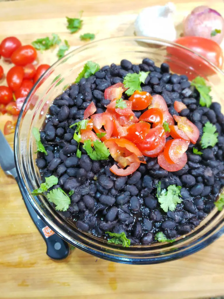 overhead image of glass bowl of cooked black beans garnished with chopped tomatoes and cilantro