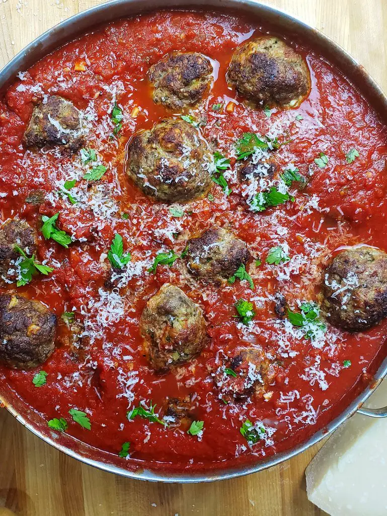 oven baked meatballs simmering in red sauce