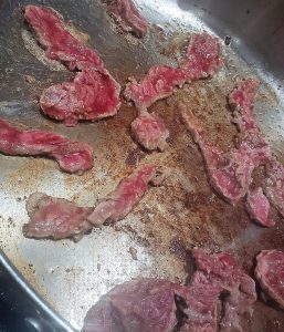 thin slices of beef searing in skillet