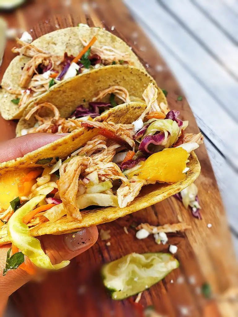 overhead view of three chipotle chicken tacos with mango slaw on a wooden board