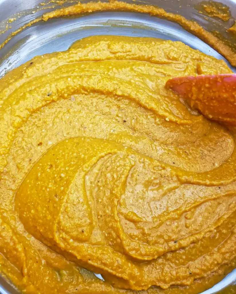 overhead image of butternut squash sauce being heated in stainless steel skillet and stirred by pink spatula