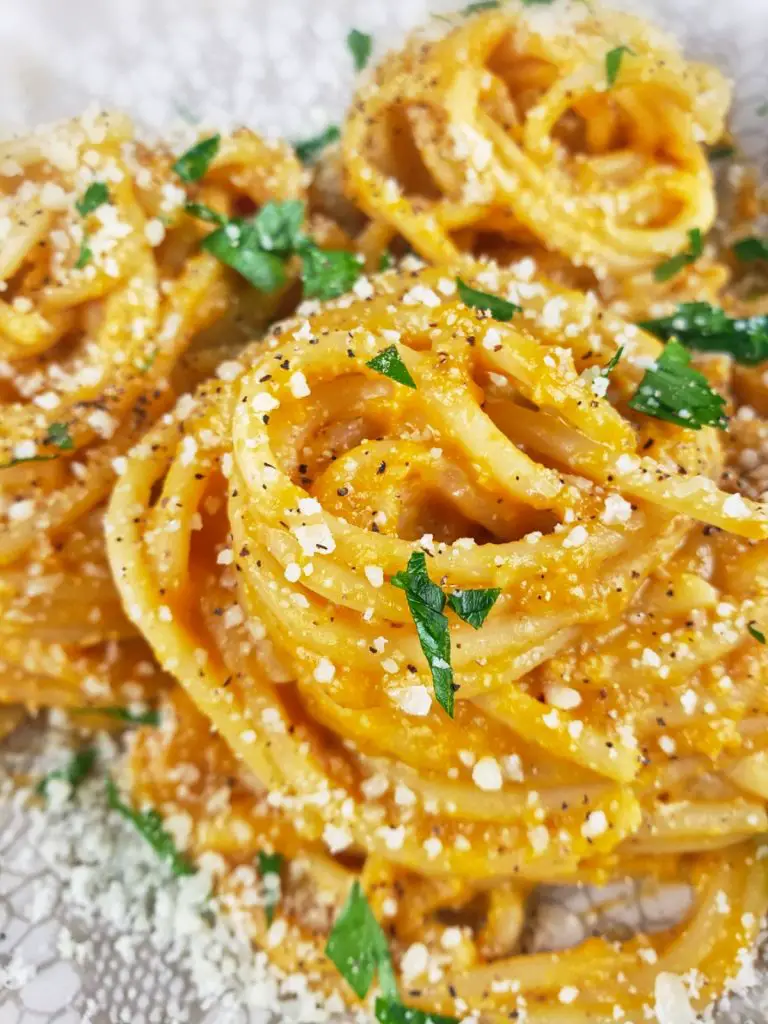 close up side image of spaghetti twirled into nests with creamy butternut squash sauce. sprinkled with parmesan cheese and chopped parsley