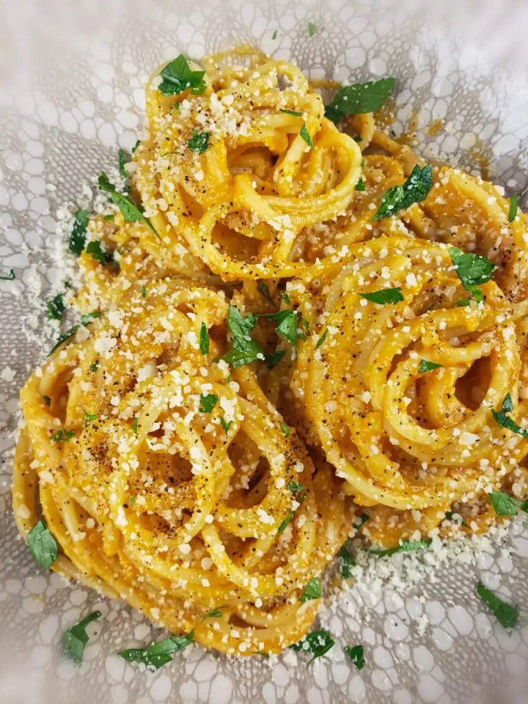 overhead image of spaghetti twirled into nests with creamy butternut squash sauce. sprinkled with parmesan cheese and chopped parsley