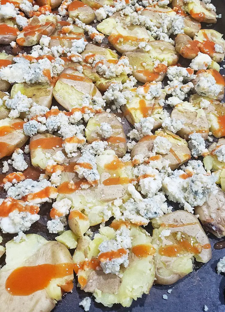 smashed teeny tiny potatoes on a sheet pan with blue cheese crumbles drizzled with buffalo sauce