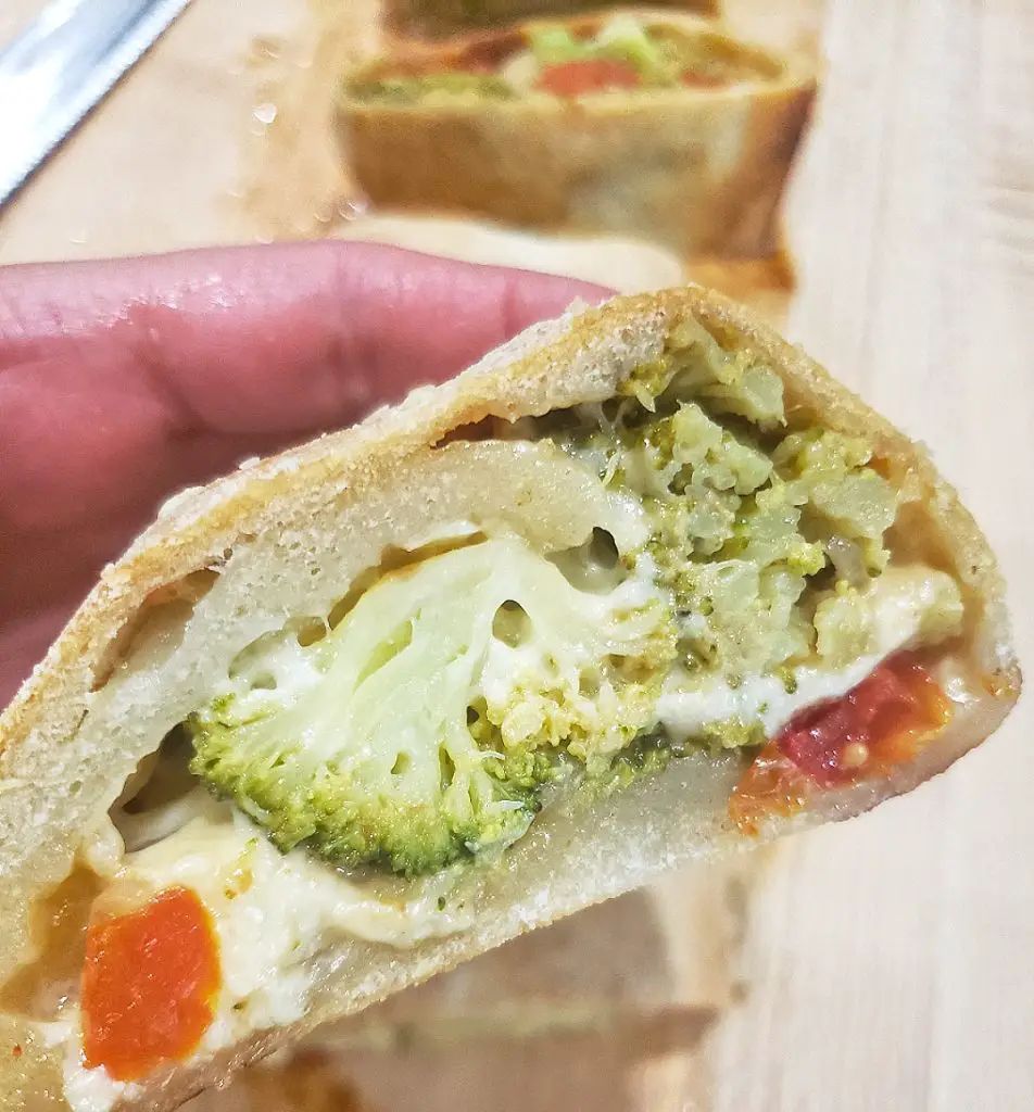 hand holding broccoli and tomato stromboli slice