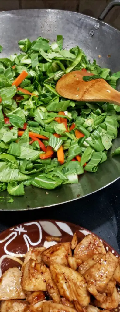 wok with vegetables and seared chicken on a plate to the side