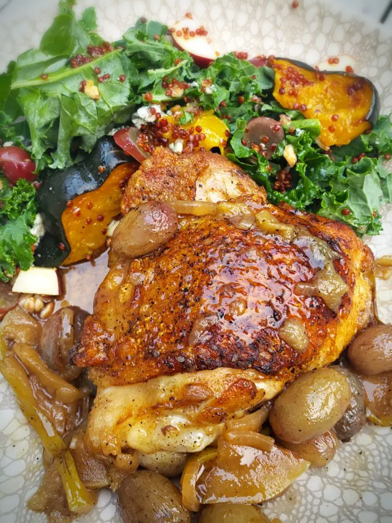 crispy cast iron seared chicken thigh with roasted grapes and apples on a plate with a kale salad
