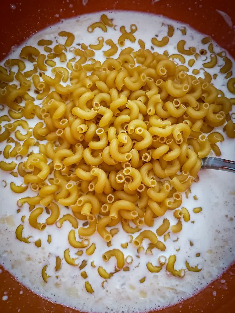 overheard image of raw pasta added to mixing bowl with milk and cheese