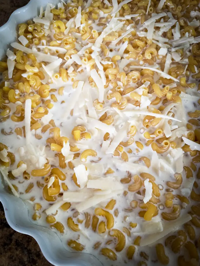image of dry pasta mixed with shredded cheeses and milk in baking dish