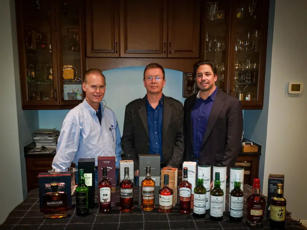 simon brookings, ken zimmerman, and lawrence lanzilli standing behind row of upscale scotch bottles