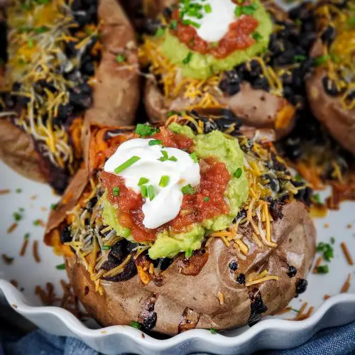image of baking dish of black bean enchilada stuffed sweet potatoes topped with guacamole salsa and sour cream