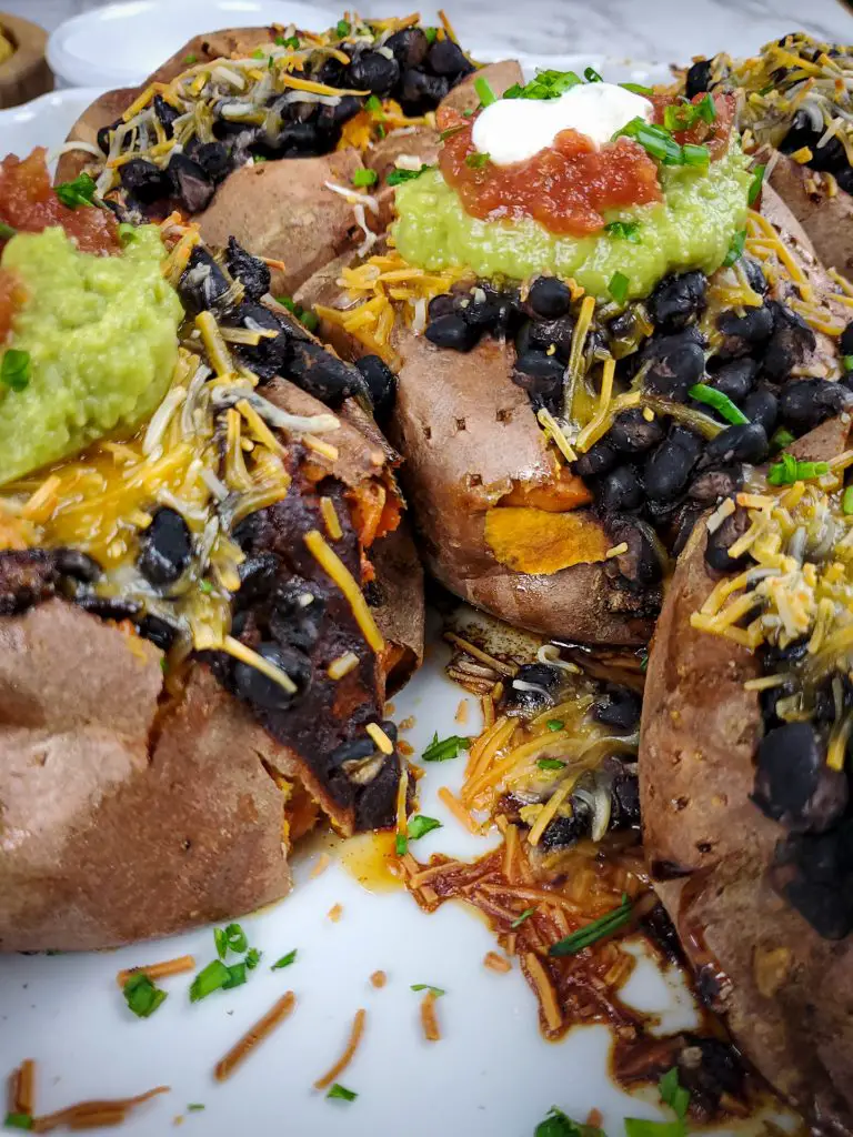 image of baking dish of black bean enchilada stuffed sweet potatoes topped with guacamole salsa and sour cream