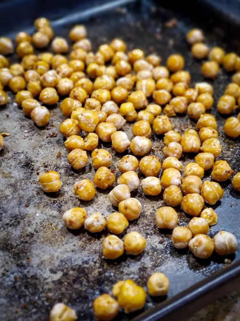 close up image of roasted crispy chick peas with chili lime seasoning on baking sheet