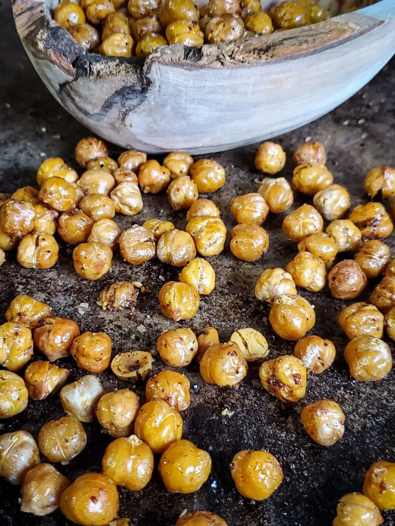 up close image of baking sheet of crispy chick peas next to a wooden bowl of chick peas