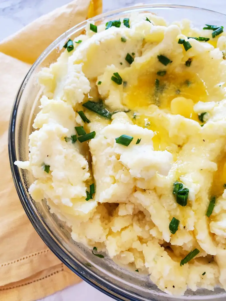 upclose image of glass bowl of yukon gold mashed potatoes with irish butter, greek yogurt garnished with chives