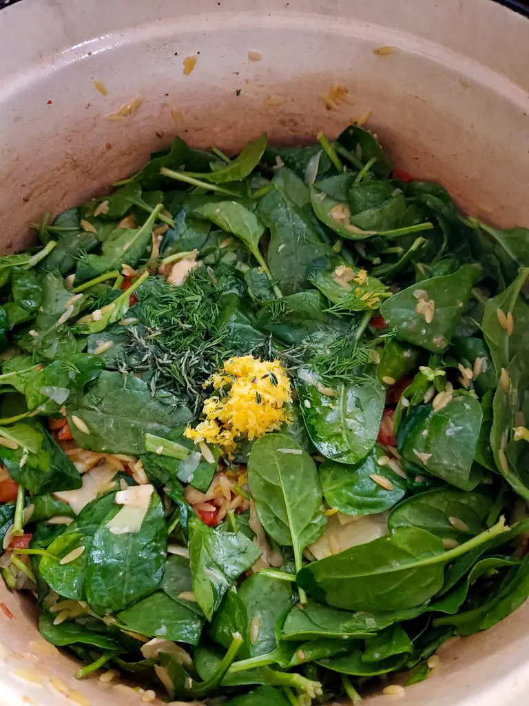 image of spinach leaves with lemon zest, fresh herbs, orzo and vegetables in dutch oven 