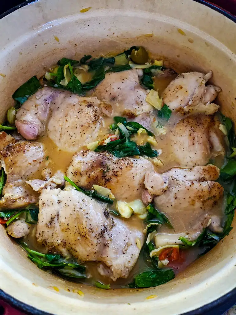 image of large dutch oven with chicken stock and greek spinach, tomatoes, olives and artichoke hearts ready to cook in oven