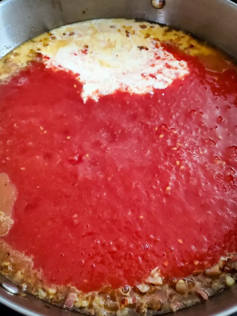 image of crushed tomatoes and cream added to shallots and pancetta for vodka cream sauce
