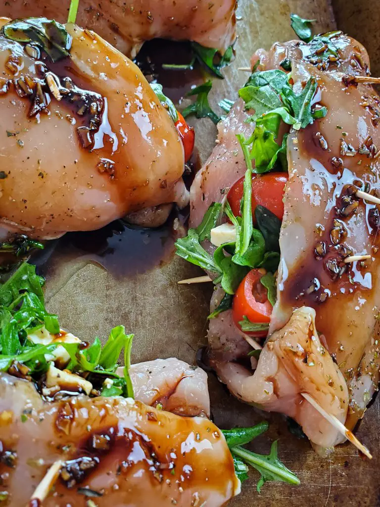 upclose image of image of raw caprese stuffed chicken breasts with balsamic glaze topped on baking sheet