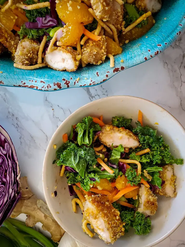 bowl of Chinese Salad with Peanut-Crusted Chicken Tenders next to large salad bowl of Chinese Salad with Peanut-Crusted Chicken Tenders