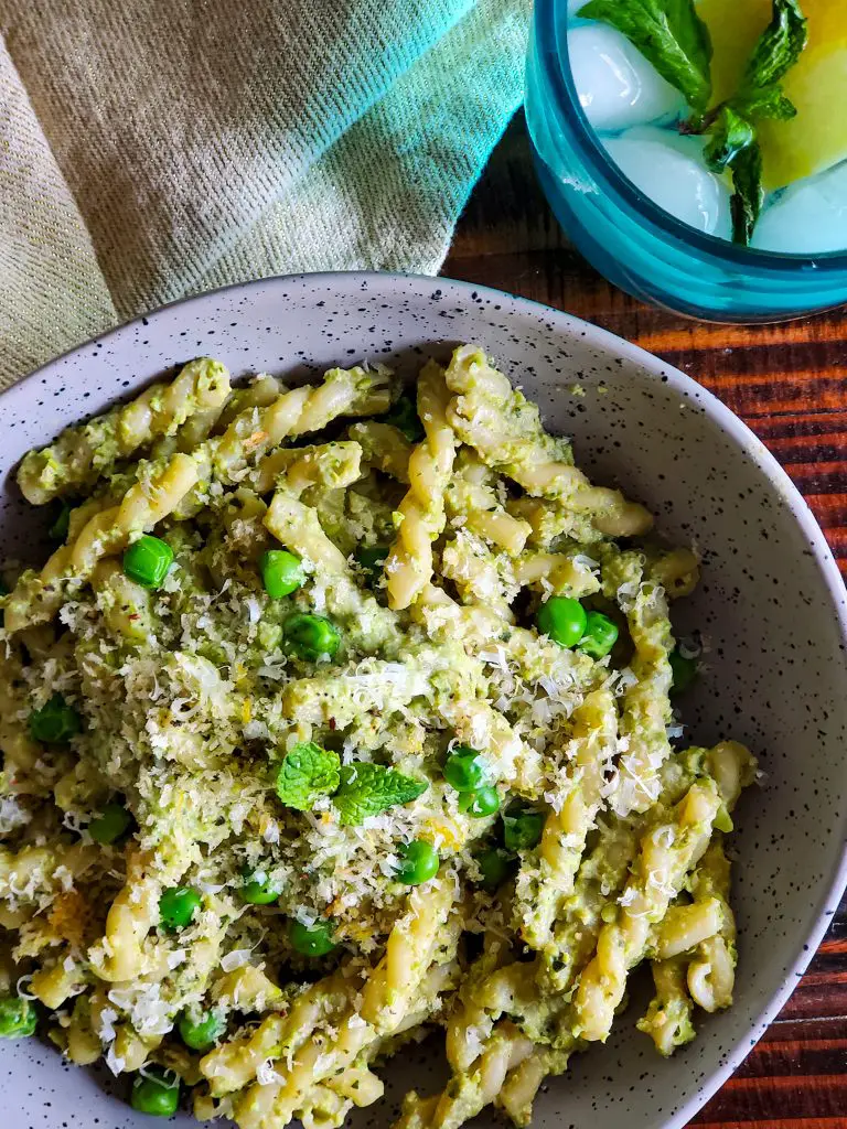 flat lay image of bowl of pea and mint pesto pasta with napkin and glass of lemon mint water