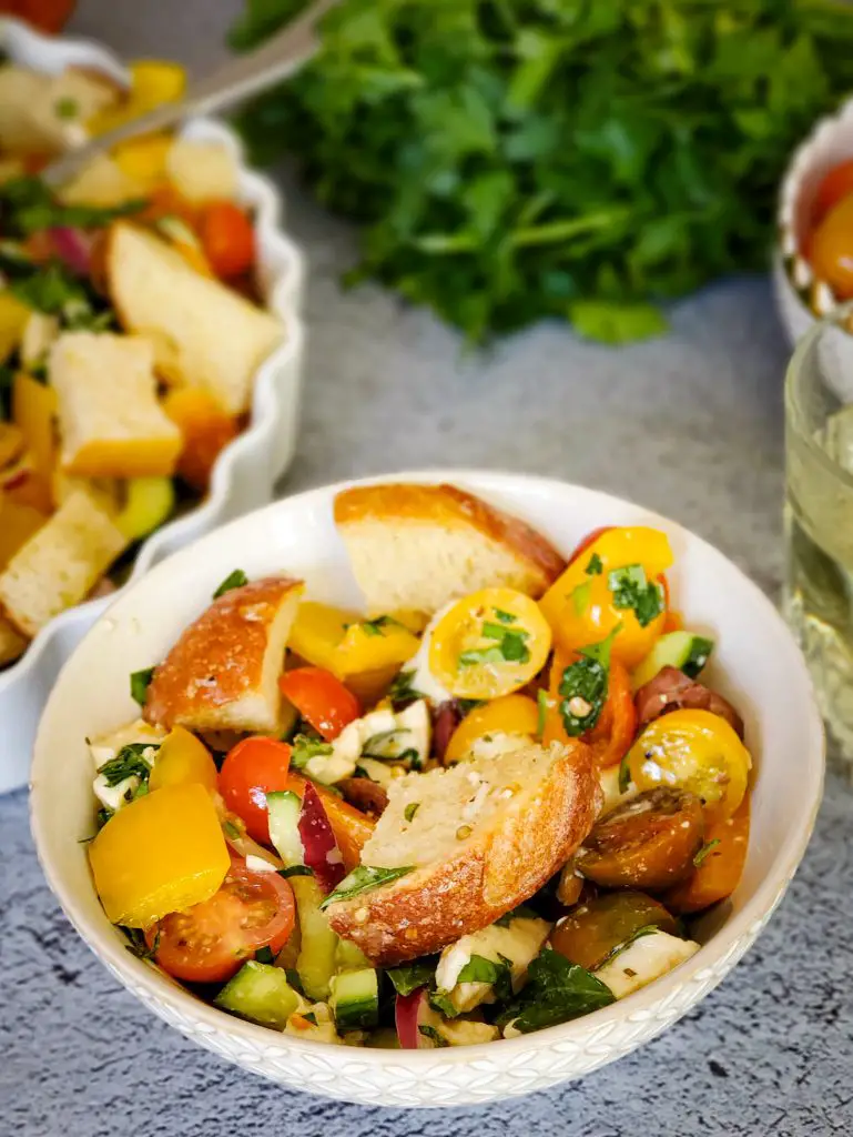 small bowl of "panzanella salad" next to salad bowl and fresh herbs