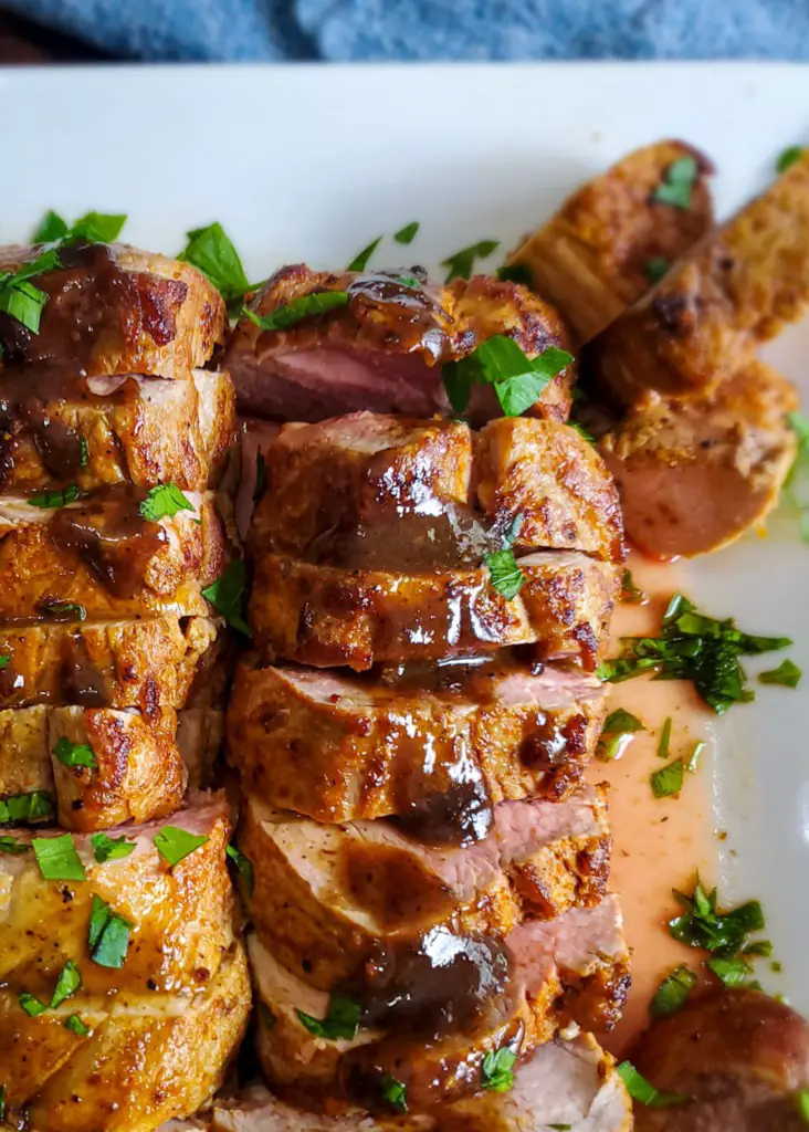 sliced roasted pork tenderloin with pan sauce on white platter