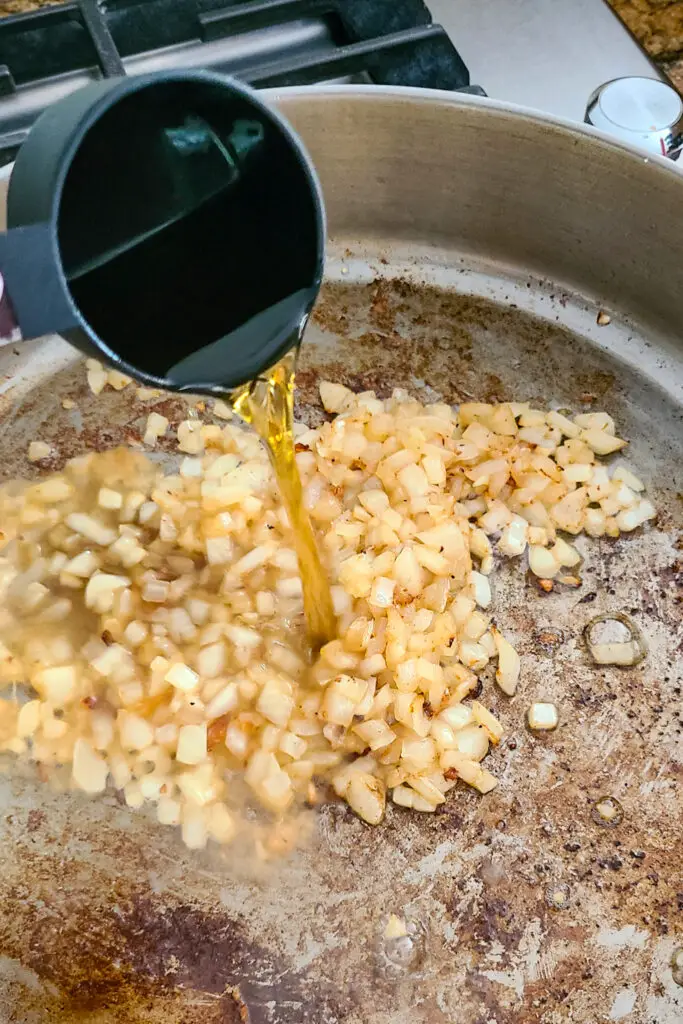 image of measuring cup of bourbon being poured over sautéd chopped onions in skillet