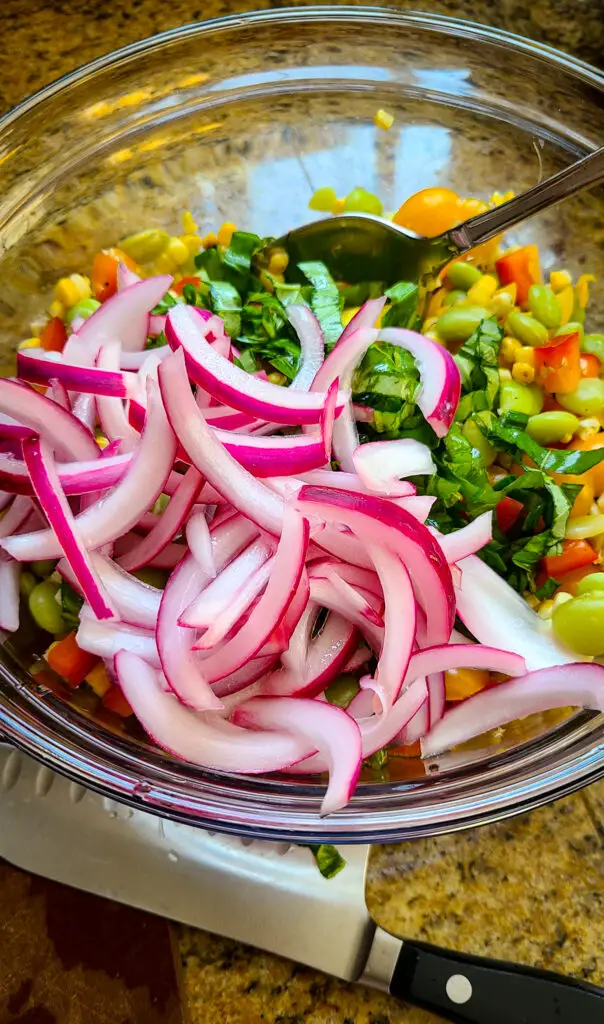 salad bowl with sliced red pickled onions over lima beans, tomatoes, grilled corn, and fresh basil