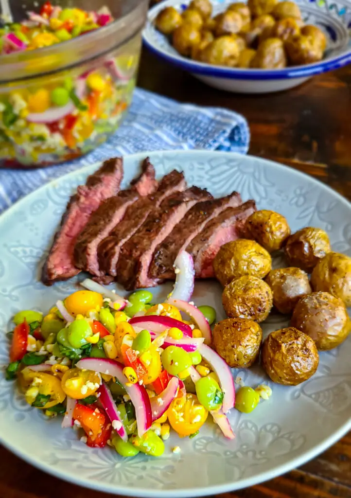 side dish of lima bean and grilled corn salad with pickled onions on a plate with grilled steak and potates