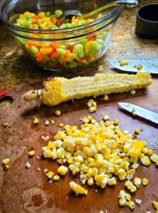 Remove grilled corn kernels from cob on cutting board with knife
