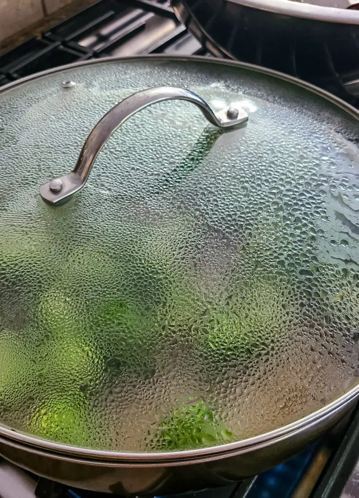 image of steaming broccoli and sugar snap peas in skillet with cover on top for the purpose of making chicken and vegetable stir fry
