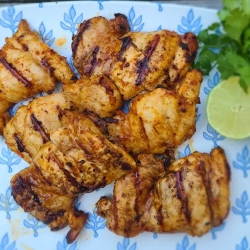 grilled chipotle lime chicken on a white plate with blue design next to a sprig of cilantro and lime