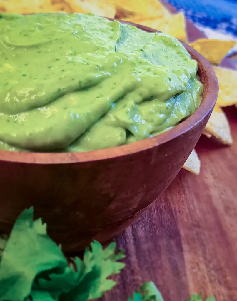 image of a side view close up of a creamy whipped guacamole in a small wooden bowl with a handful of tortilla chips next to the guacamole