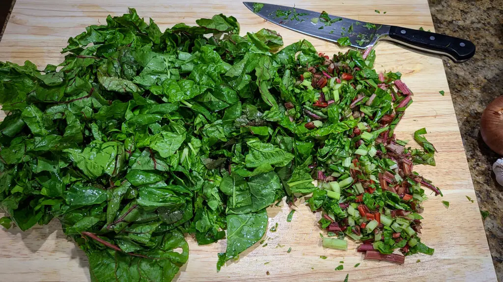 overhead image of swiss chard greens on large wooden cutting board. the leaves are sliced into stips and the stems have been removed and chopped