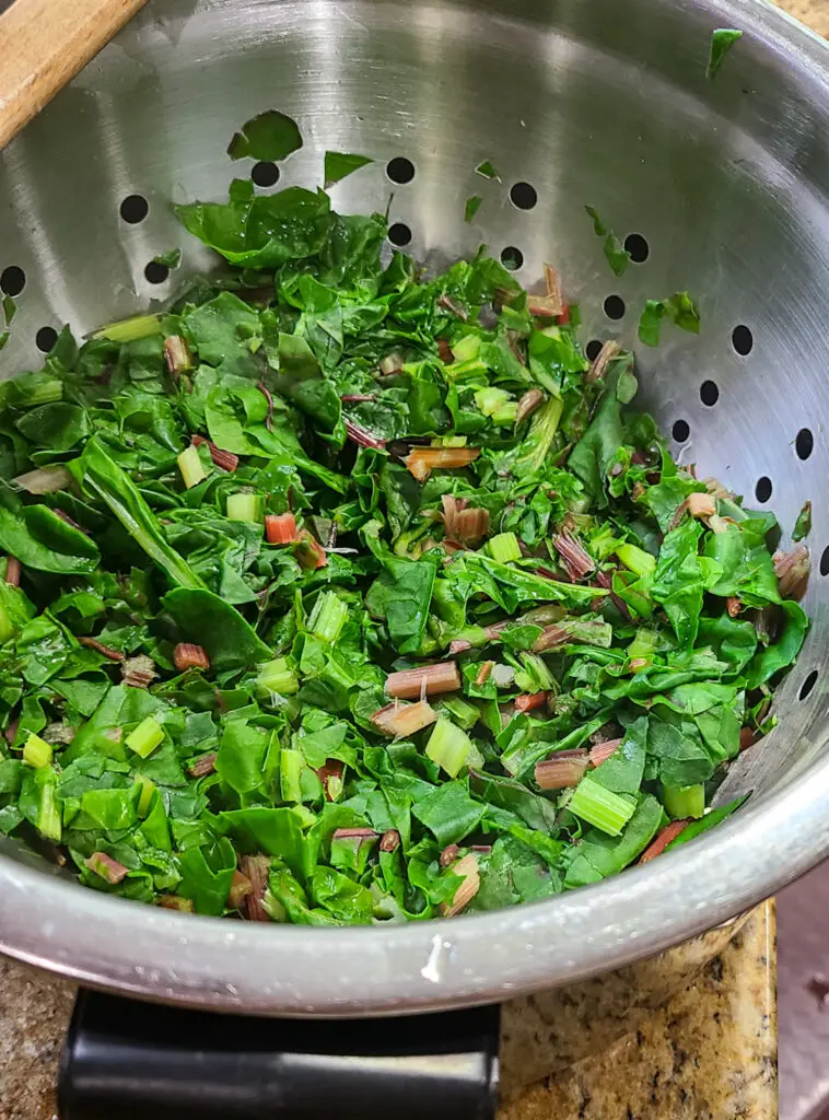 overhead image of boiled chopped swiss chard leaves drained in a colander.