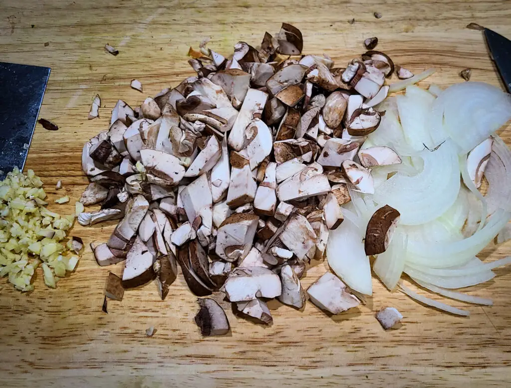 overhead image of cutting board with sliced onion, chopped baby bella mushrooms and minced garlic