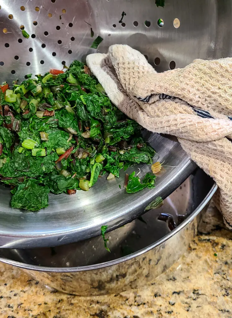 image of dish towel next to colander of boiled swiss chard leaves that have been squeeze with towel to press out excess liquid