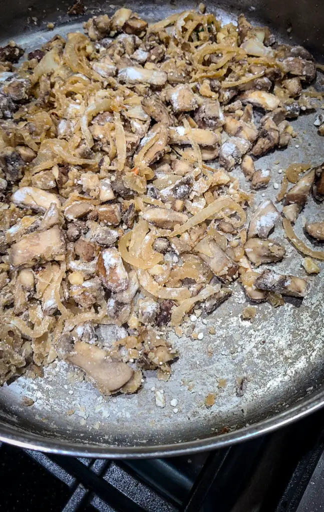Image of sautéed baby Bella mushrooms and onions in skillet with flour sprinkled over top