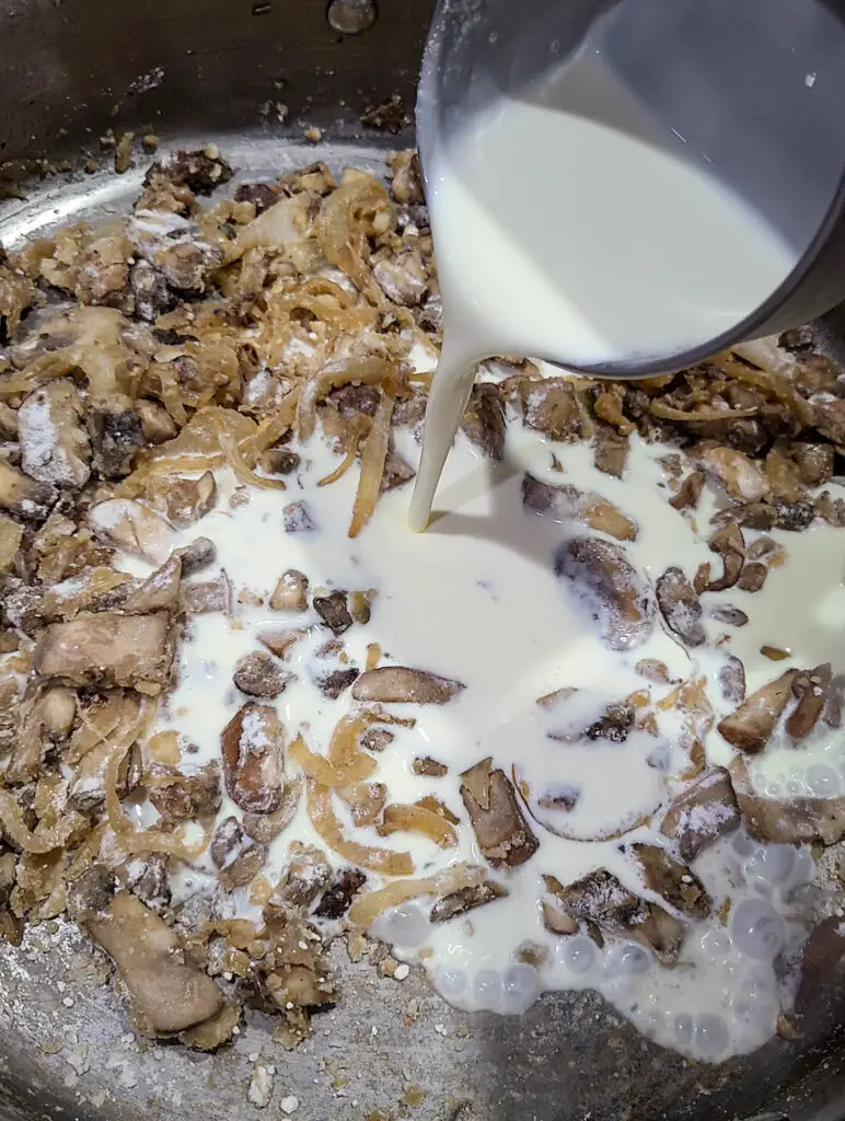 Image of sautéed baby Bella mushrooms and onions in skillet with cup of cream being poured into skillet