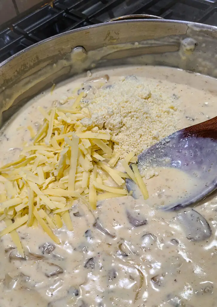 image of cream sauce with mushrooms and onions with grated cheese being stirred into it.