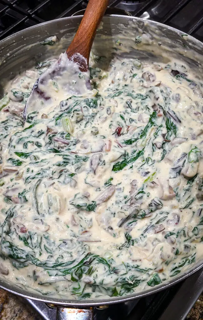 image of skillet with cream sauce with baby bella mushroom, onion, and cooked swiss chard stired into to create the base for gnocchi gratin
