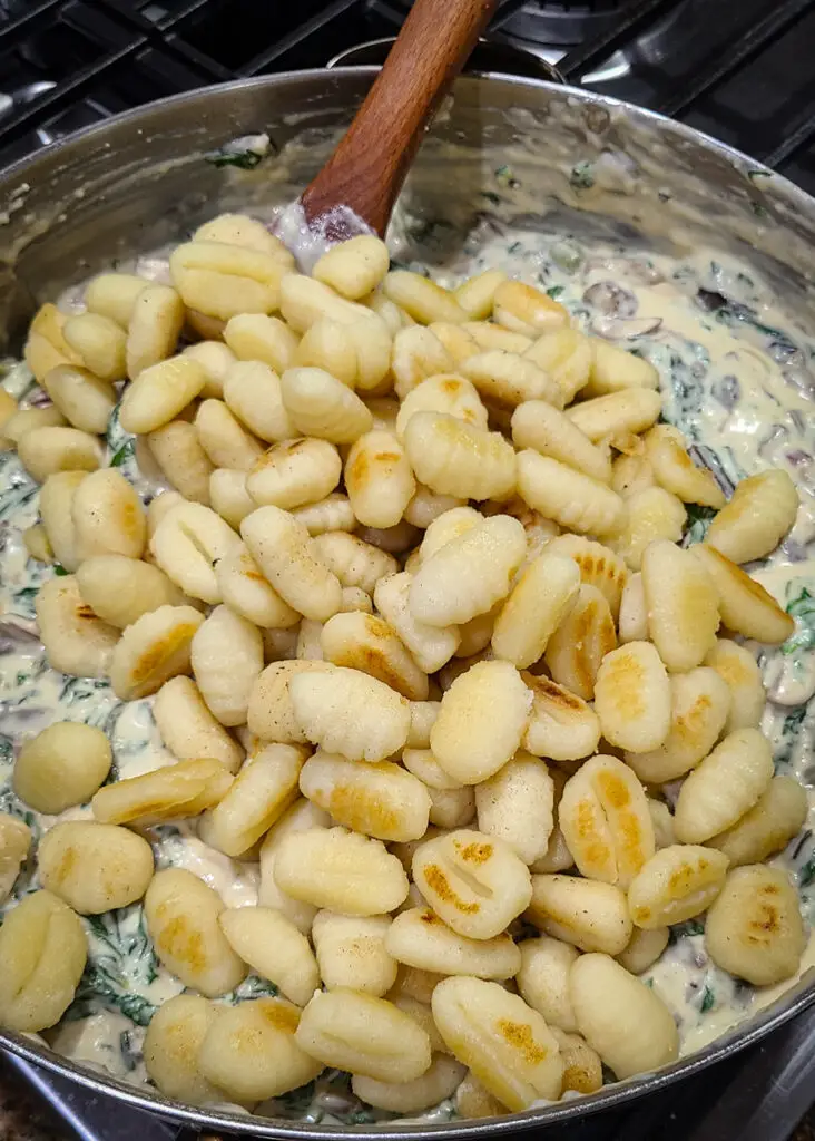 image of pan seared gnocchi being folded in to creamy and cheesy swiss chard and mushroom sauce.