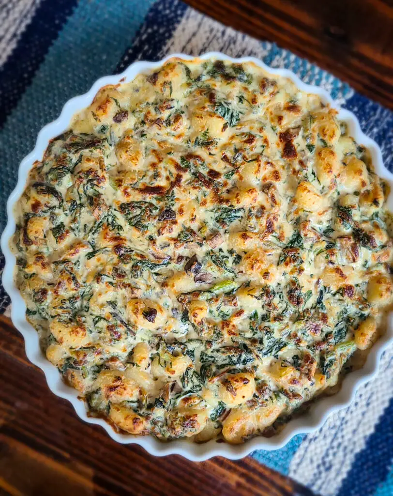 Overhead image of baked Swiss Chard and Baby Bella Gnocchi Gratin on dark wood table next to blue runner