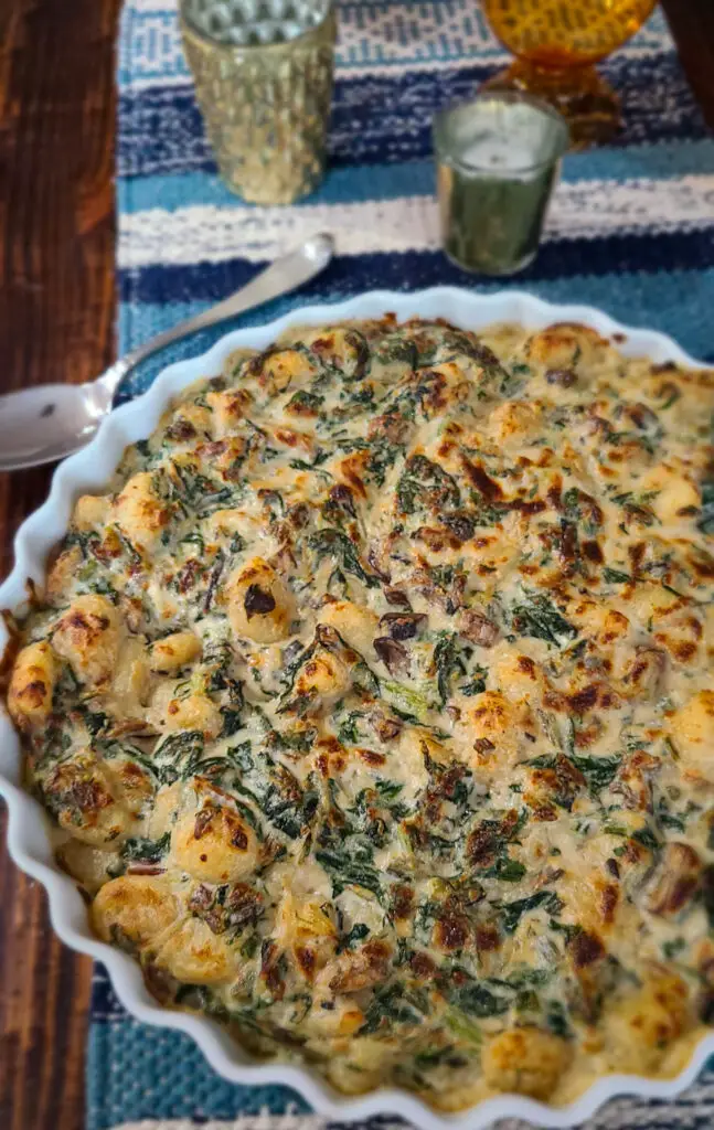 Overhead image of baked Swiss Chard and Baby Bella Gnocchi Gratin being presented on dinner table with gold votive candles and serving spoon
