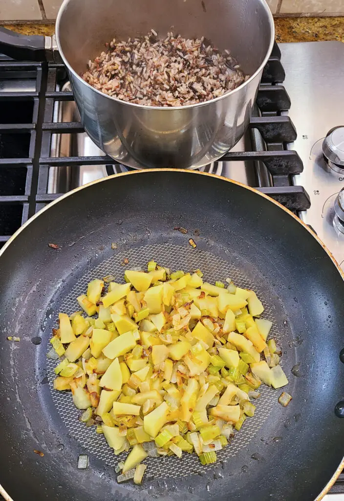 cooked wild rice medley in pot next to skillet of sauteed aromatics 