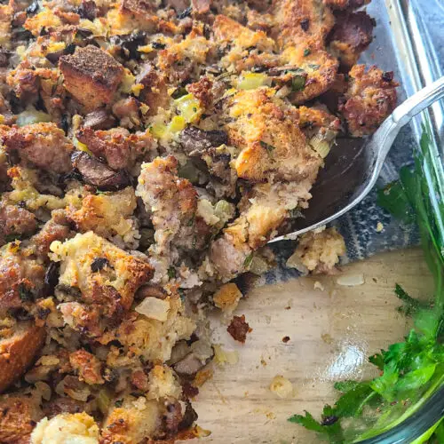 herb sourdough mushroom and sausage stuffing in glass pyrex baking dish with serving spoon