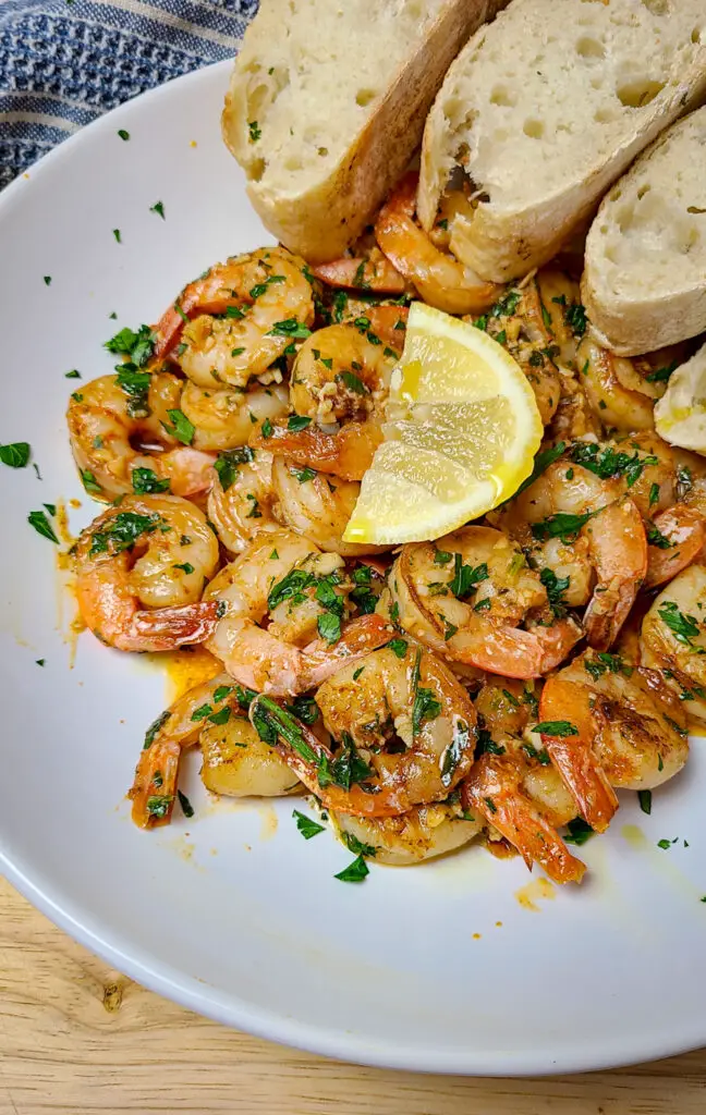 garlic butter shrimp on serving plate with slices of bread and a lemon wedge