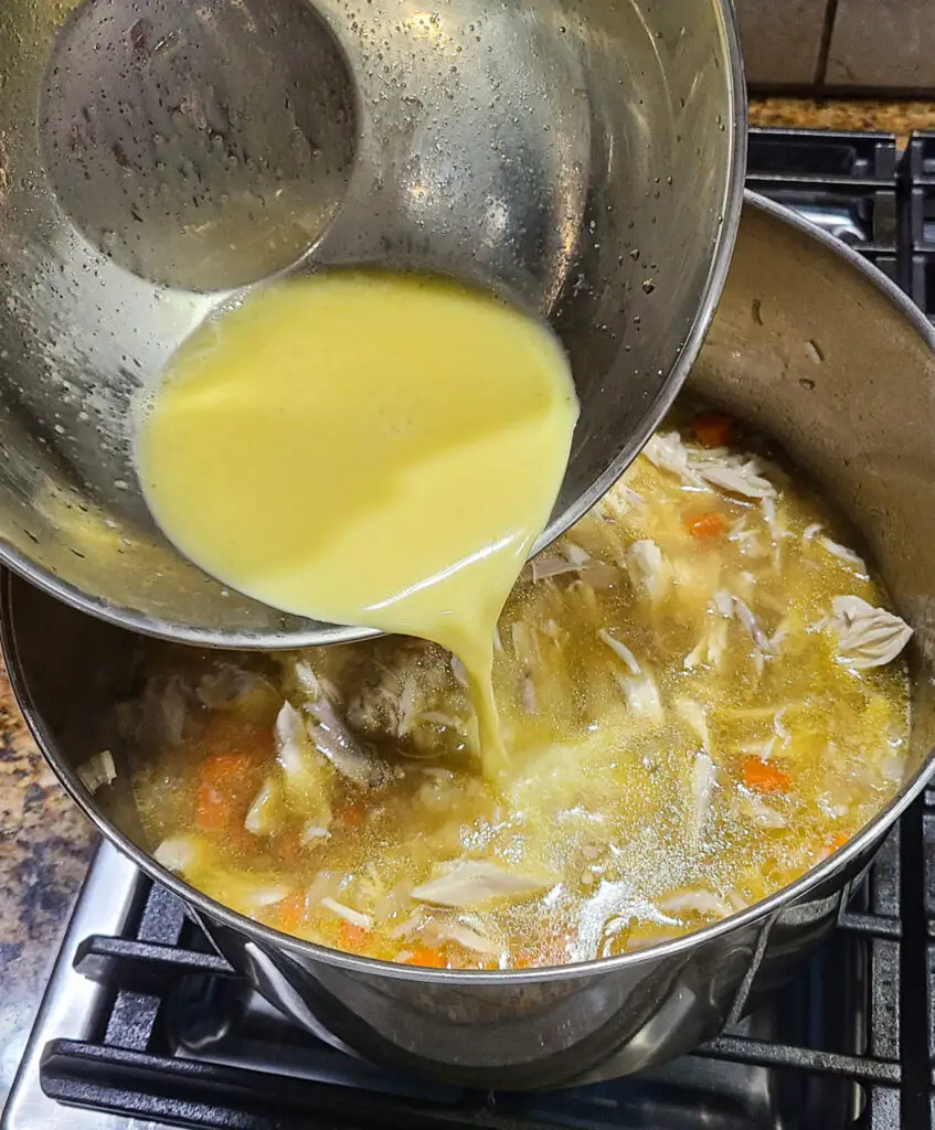 pouring tempered avgolemono sauce into large pot of chicken soup