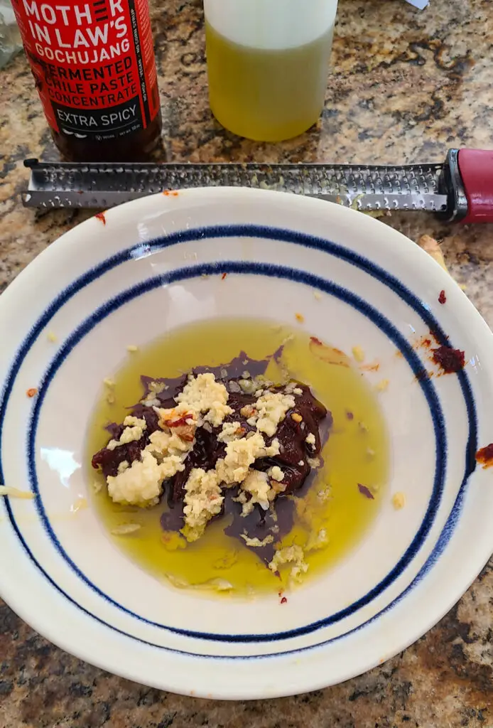 bowl showing olive oil, gochujang paste, grated garlic and ginger to make rub for roasted chicken